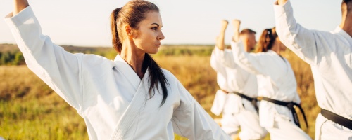 Karate group with master in white kimono, workout in summer field. Martial art training outdoor, technique practice
